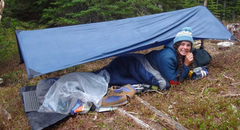 an outward bound student smiles from under their shelter while on solo